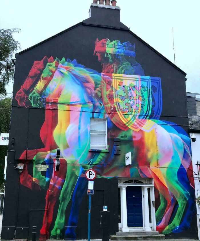 A vibrant, interesting photo of a building mural depicting a colorful knight on a horse, with a shield and multiple crowns.