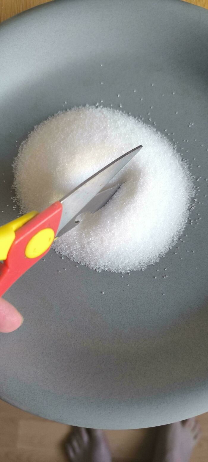 A pair of scissors cutting into a pile of white sugar on a gray plate, illustrating a not interesting moment.