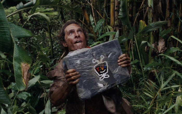 A man holding a package in a jungle, emphasizing nonsensical movie details.