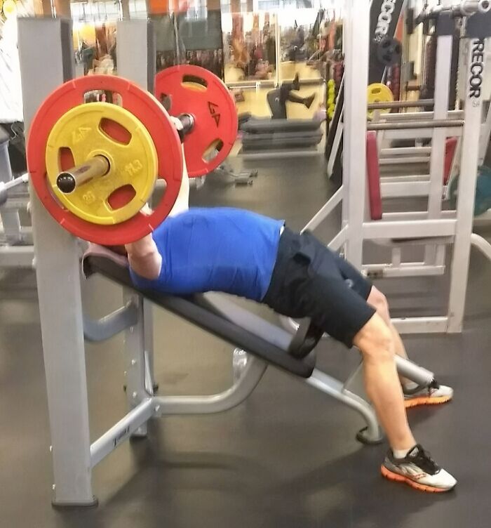 Man in blue shirt lifting heavy weights on an incline bench press at the gym in a Darwin Award contender moment.