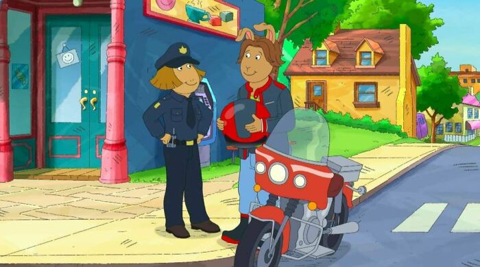 Arthur and a police officer standing next to a motorcycle, pointing out nonsensical movie details.