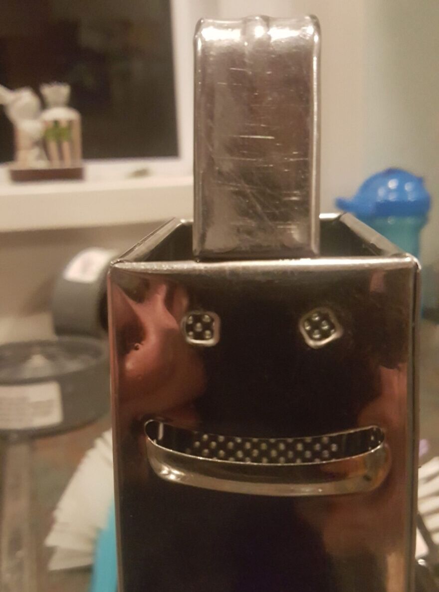 Close-up of a metallic kitchen gadget showing pareidolia with face-like holes and a smiling mouth shape.