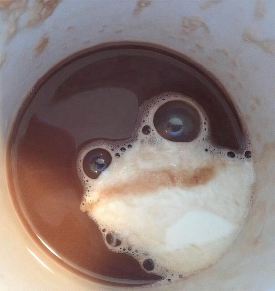 Coffee foam in a cup forming a face-like shape, a natural example of pareidolia captured in a photo.