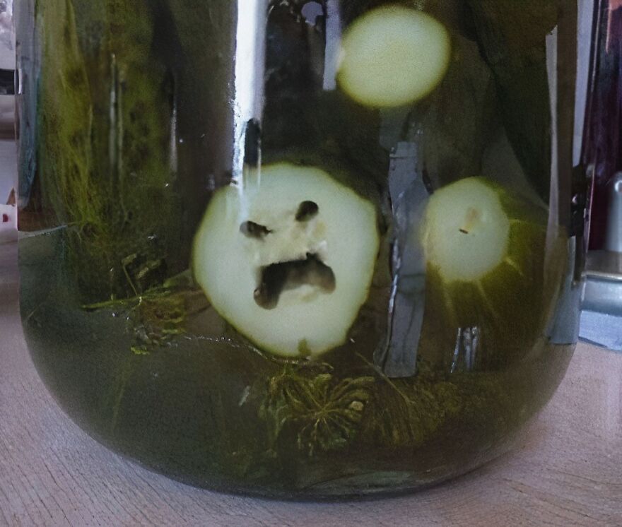 Pickle slice in jar with a pattern resembling a face, an example of pareidolia captured in a photo.