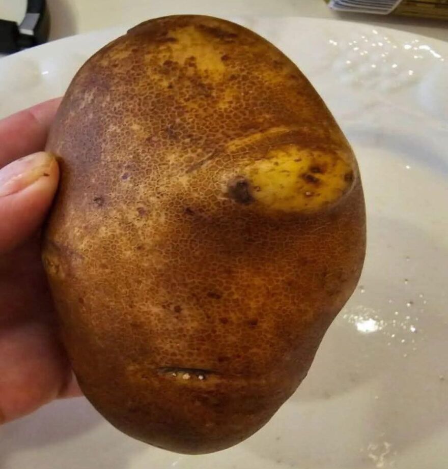 Hand holding a potato with natural markings resembling a human face, showcasing pareidolia in a close-up view.