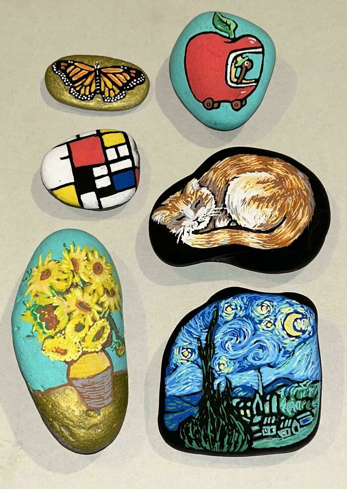 A collection of six handmade projects painted rocks, including a butterfly, an apple with a spaceman, abstract shapes, a sleeping cat, sunflowers, and The Starry Night.