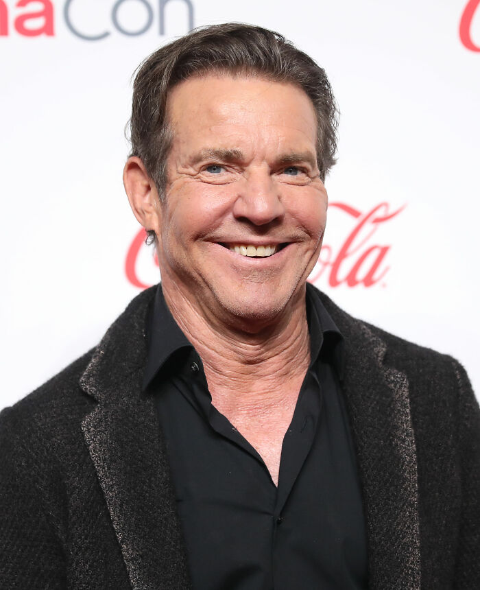 Dennis Quaid smiling at an event, wearing a black shirt and textured dark jacket, highlighting his bio and career.