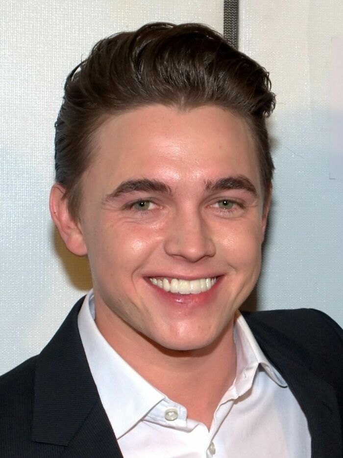 Jesse McCartney smiling at an event, wearing a black suit jacket and white shirt, highlighting his career in entertainment.
