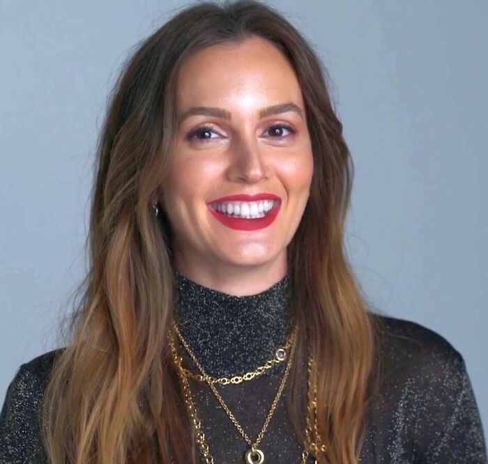Leighton Meester smiling, wearing a sparkly black top and layered gold necklaces in a neutral studio setting.