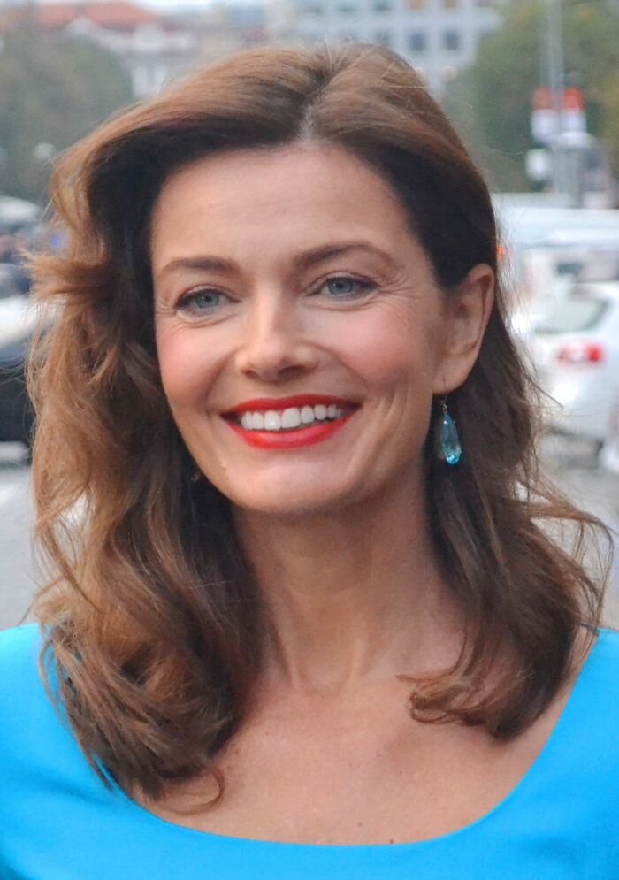 Paulina Porizkova smiling outdoors with wavy hair, wearing blue top and turquoise earrings, showcasing career highlights.