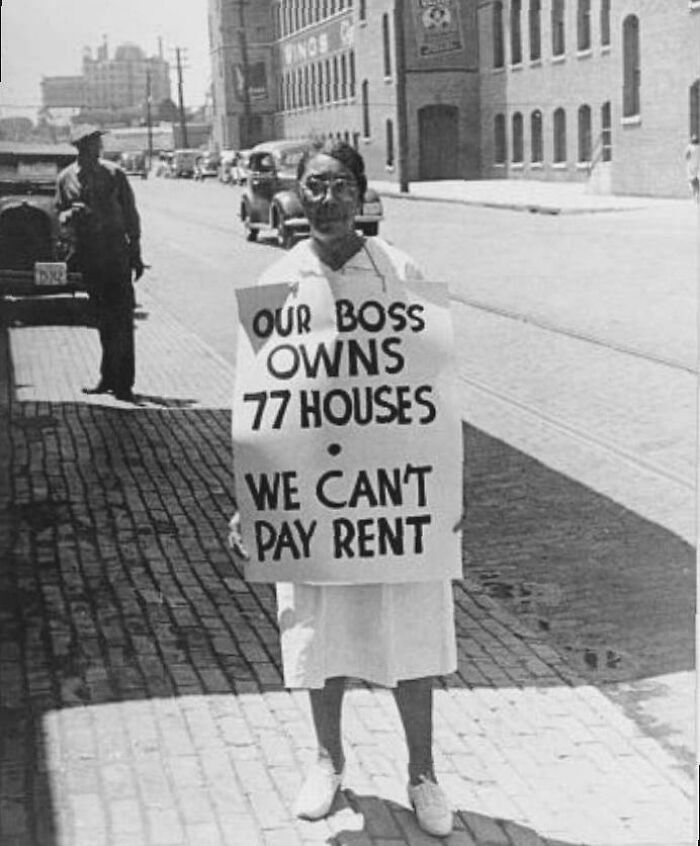Woman in historic photo protesting rent with sign about boss owning 77 houses, illustrating life in a different era.