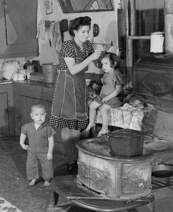 Woman caring for children in a rustic kitchen, a rare and fascinating historic photo showing daily life in a different era.