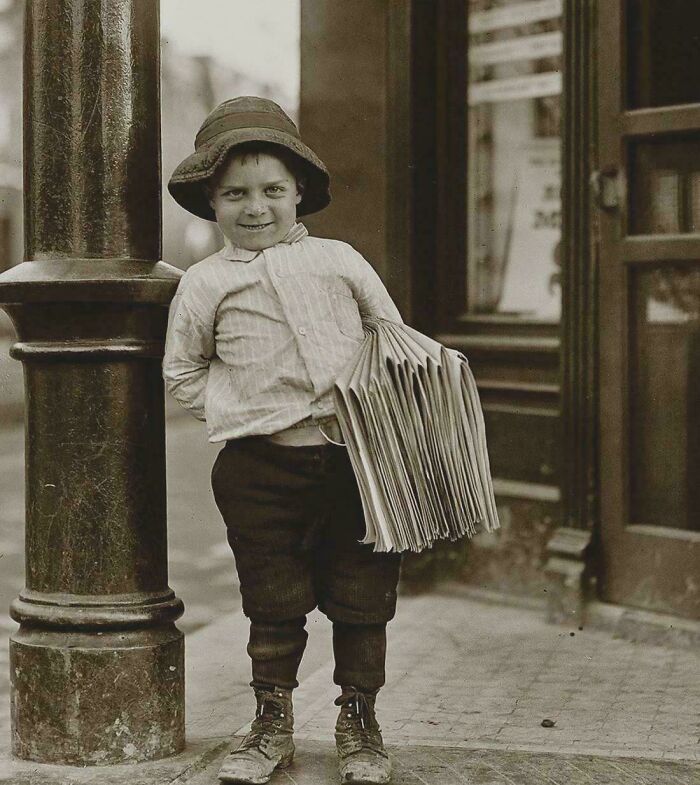 Young boy selling newspapers on a street corner in a rare and fascinating historic photo capturing life in a different era.