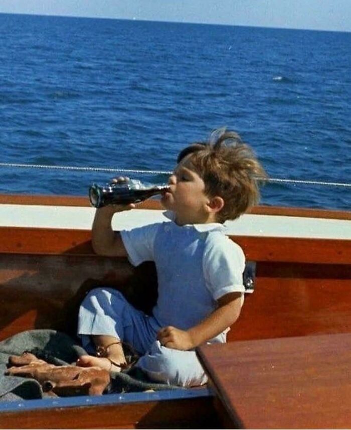 Child on boat drinking soda from glass bottle historic photo capturing life in a different era by the sea.