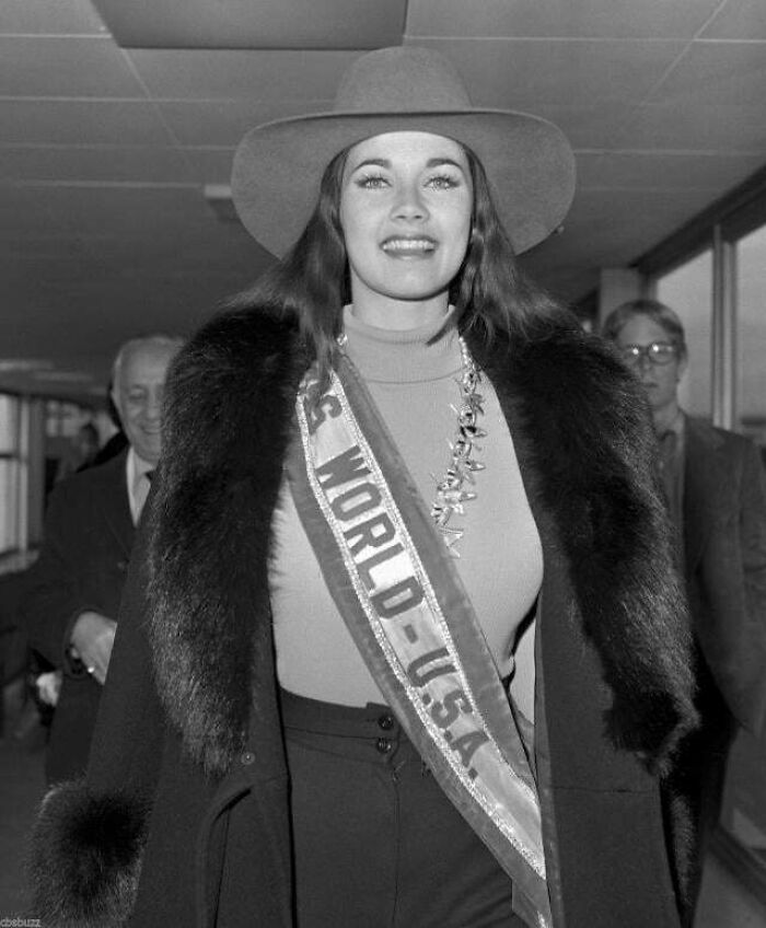 Black and white historic photo of a smiling woman wearing a sash and fur coat, capturing rare life moments from a different era.