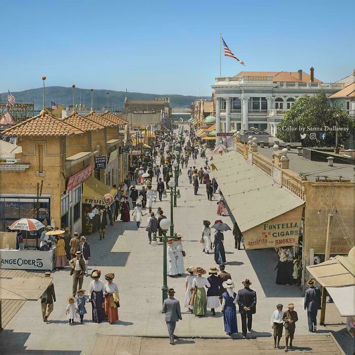Crowded historic street scene with men, women, and children dressed in early 20th-century attire in a vibrant era.