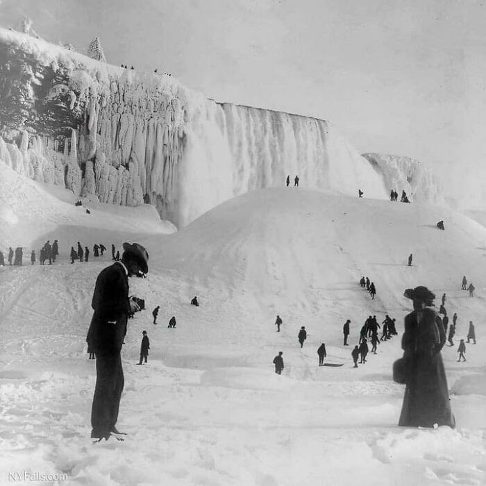 Historic photo of people exploring a snowy frozen waterfall landscape, offering a glimpse into life in a different era.