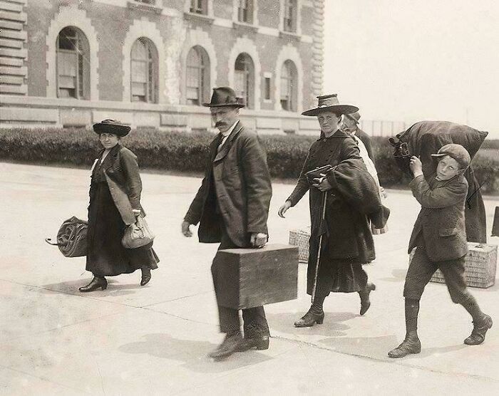 Family carrying luggage and walking outside a historic building in a rare and fascinating historic photo capturing life in a different era
