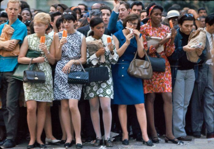 Group of women in vintage 1960s dresses eating ice cream on a crowded street, rare historic photo capturing life in a past era