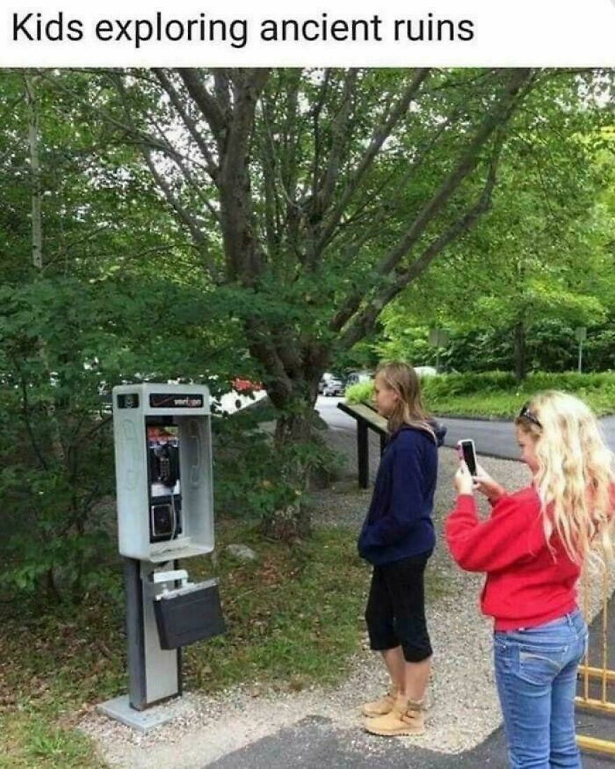 Two girls examining an old payphone outdoors, illustrating 80s posts about parts of our lives that don’t exist anymore.