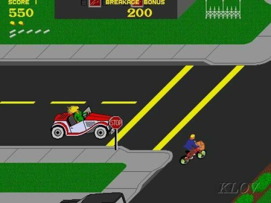 Screenshot of an 80s retro arcade video game showing a car and a bicyclist at a street intersection with pixelated graphics.