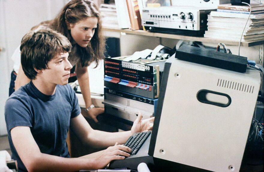 Two teenagers using an old computer and vintage tech equipment, illustrating 80s parts of life that no longer exist.