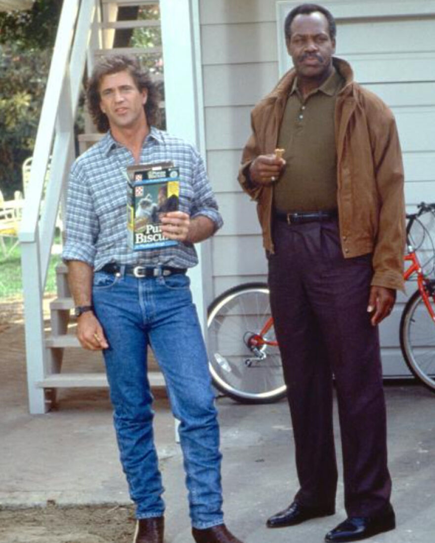 Two men in 80s casual clothing standing outside by a bike, reflecting parts of 80s life that don’t exist anymore.