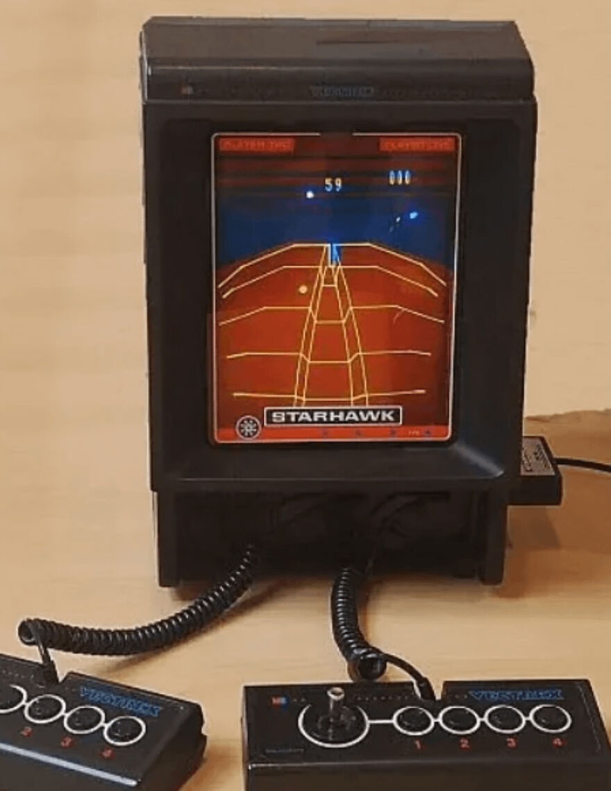 Vintage 1980s video game console with wired controllers showing pixelated graphics of a tennis-like game scene.