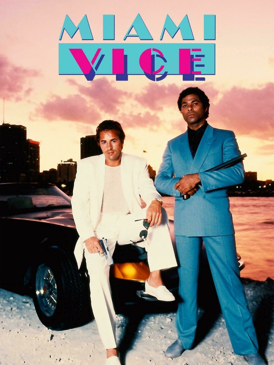 Two men in 80s style suits posing with guns by a car at sunset, reflecting 80s posts about parts of life gone.