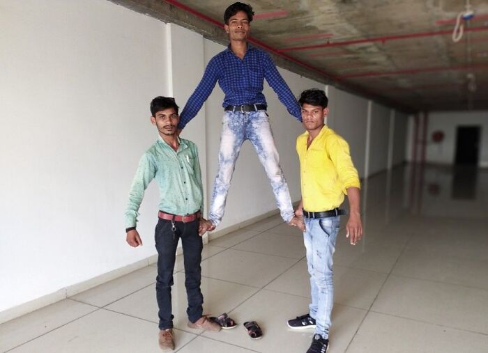 Three men striking creative and hilarious poses, with one being lifted off the ground by the other two indoors.