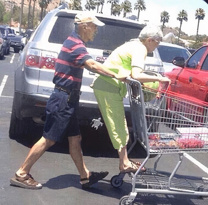 Elderly couple having fun in a parking lot with one riding a shopping cart in a lighthearted safe-for-work moment