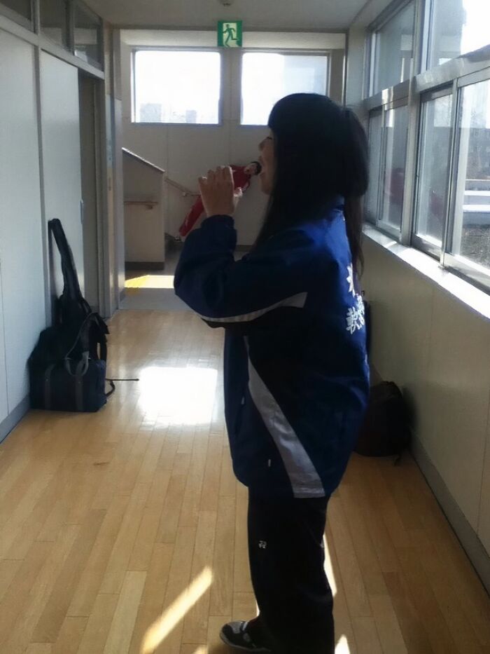 Person creatively posing in hallway, appearing to drink from a small figure, showcasing hilarious and creative poses.