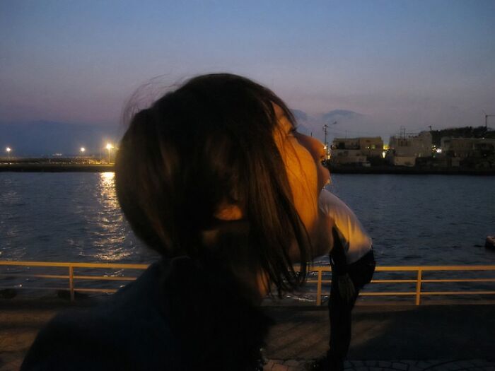 Person at waterfront at dusk creatively posing to appear as if about to eat another person in the distance.