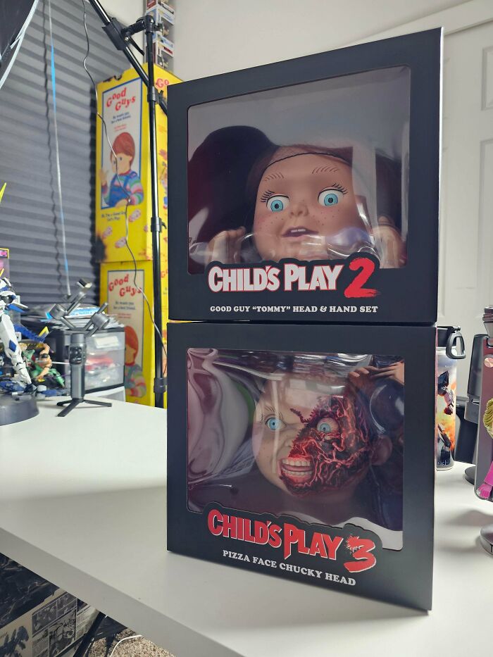Two boxed Child's Play 2 and 3 collectible heads displayed on a white table, linked to strange elevator pit discoveries.