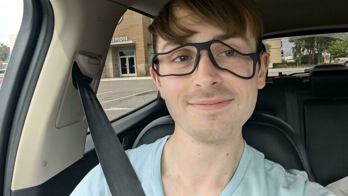 Young man wearing glasses and a seatbelt, smiling in a car, illustrating gut warnings about something horrible experiences.