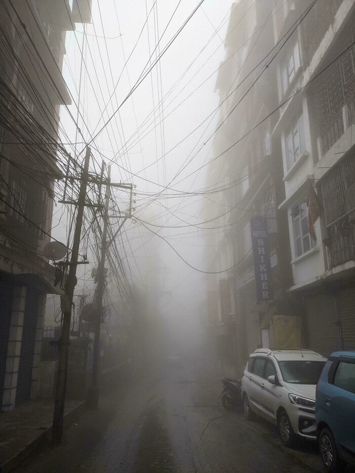 Foggy urban street with tangled electric wires and cars parked alongside