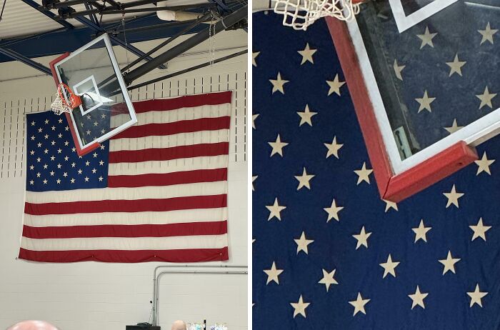 An American flag hanging behind a tilted basketball hoop in a gym, an upside-down thing needing fixing.