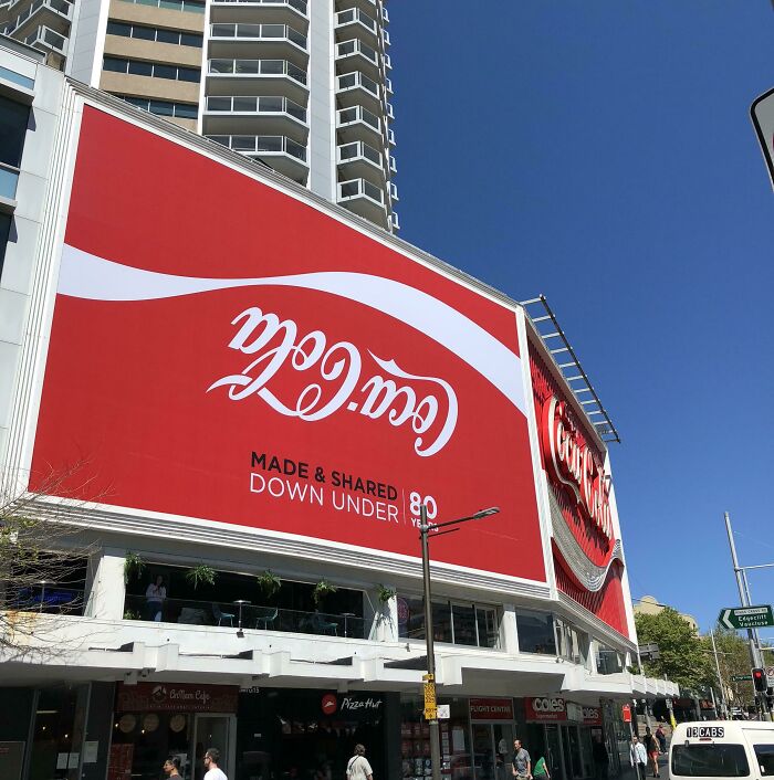 A large, upside-down Coca-Cola sign on a building in a city, making you want to fix this weird thing.