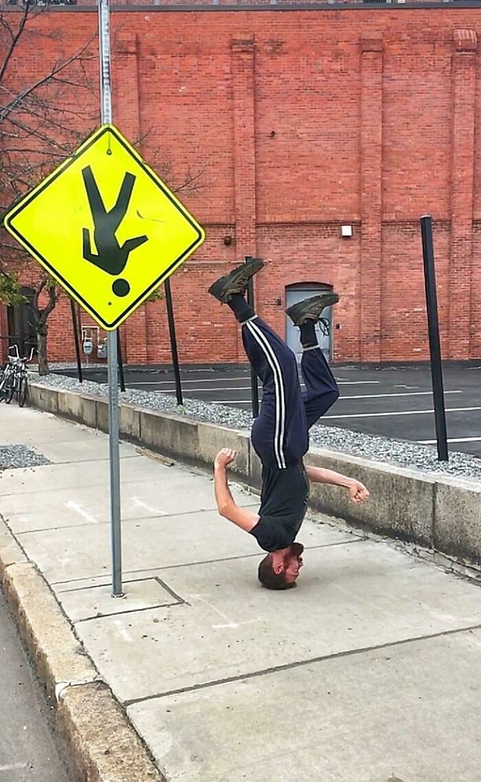 A man does a headstand next to a yellow upside-down pedestrian sign, fixing the weird perspective of the world.