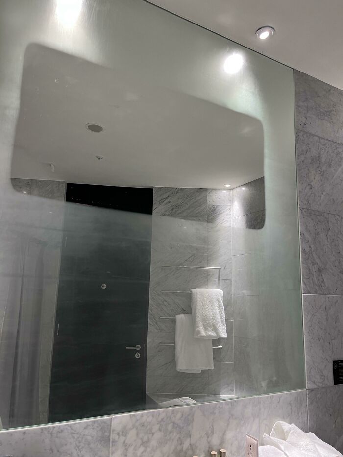 A modern bathroom with a large mirror reflecting marble walls and white towels on a rack, highlighting upside-down things.