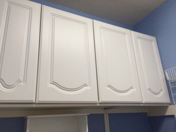 Four white kitchen cabinets against a blue wall, featuring a decorative inverted curve design that looks upside-down.