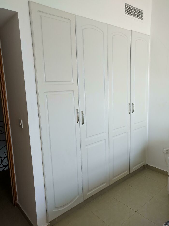 White built-in wardrobe with textured doors and metal handles, showing a ceiling vent. Might make you want to fix things.