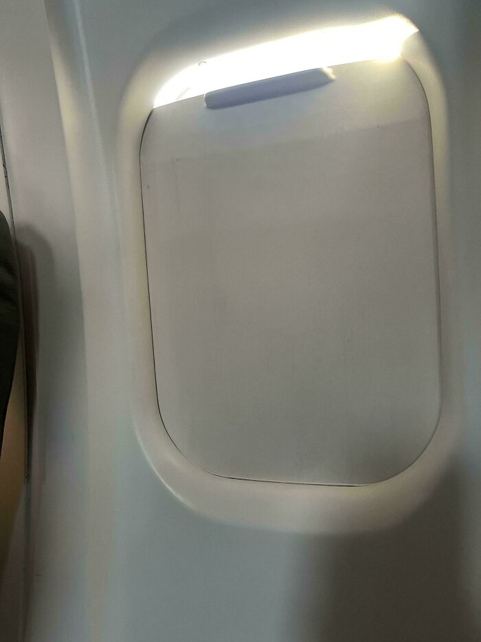 An airplane window with the shade pulled down, showing a slight glow from outside. A weird upside-down thing.