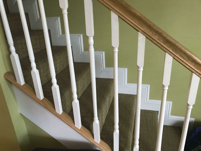 A carpeted staircase with white balusters and a wooden handrail against a light green wall. Fix weird things.