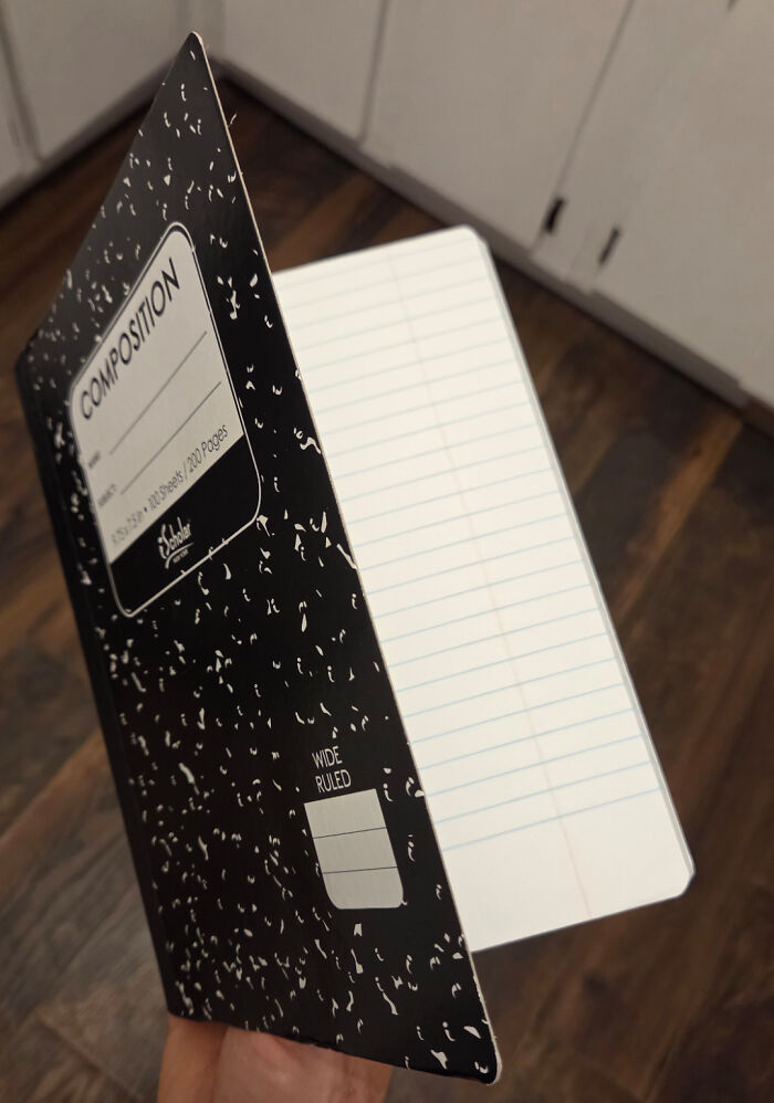 A person holds an upside-down composition notebook, showcasing its wide-ruled pages, a prime example of upside-down things.