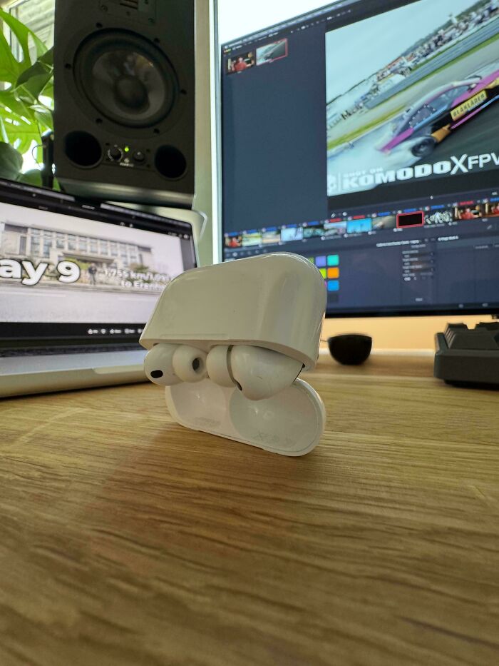 White AirPods case on a wooden desk with a laptop and monitor, one of many upside-down things to fix.