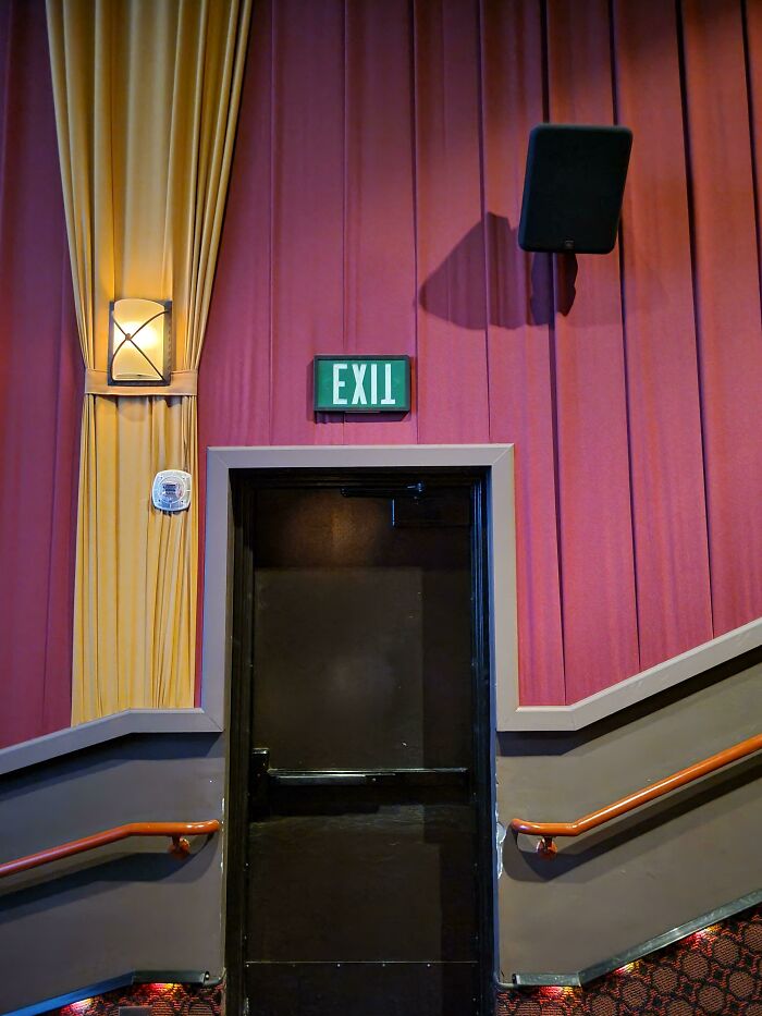 A dark exit door with a green EXIT sign above it, flanked by red and gold curtains. This might be one of those weird upside-down things.