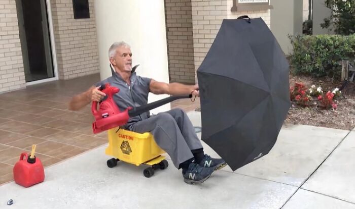 Man using leaf blower to hold umbrella while sitting on yellow caution bucket, illustrating gut warning signs about something horrible