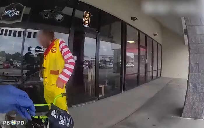 Person in colorful costume standing outside a storefront, showing a gut warning moment captured by police body camera.