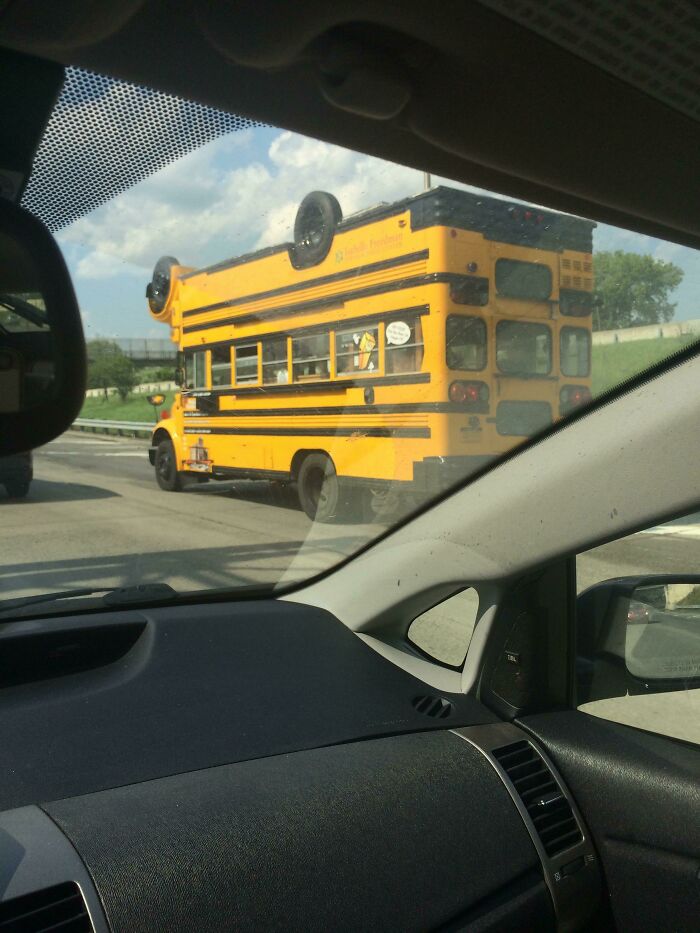 A yellow school bus is designed to look upside-down, complete with tires on its roof, a truly weird upside-down thing.